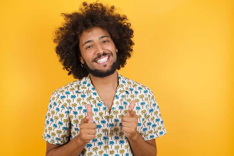 Cannabis Strain Effects - Young man with afro hair over wearing hawaiian shirt standing over yellow background pointing fingers to camera with happy and funny face. Good energy and vibes.